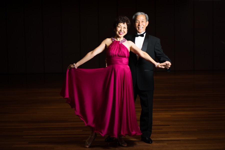 A longtime HBDA couple in a magenta gown and tuxedo smiling on stage