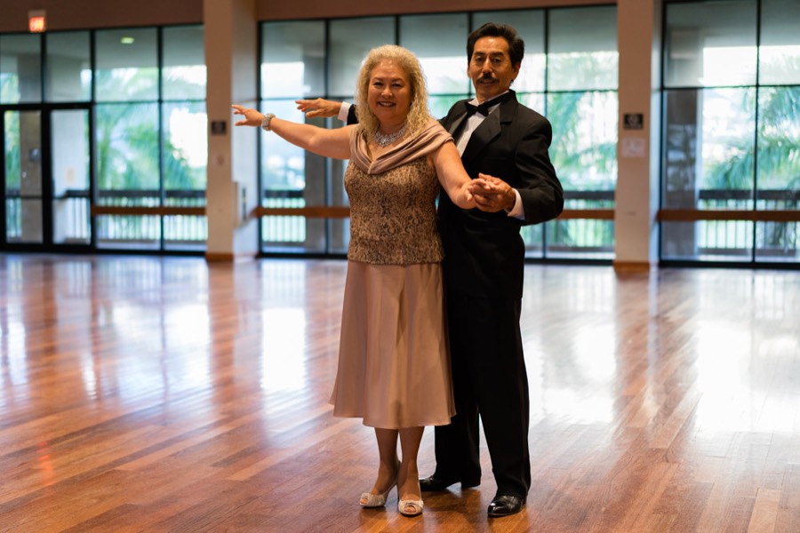 A smiling couple in everyday dress practicing a dance hold in a sunny hall