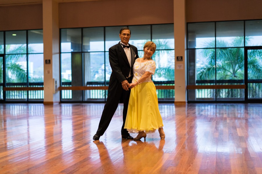 A couple in a yellow dress and tuxedo posing mid-dance in a bright hall