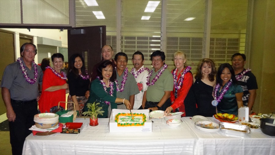 A group of HBDA members wearing leis gathered around a celebration cake
