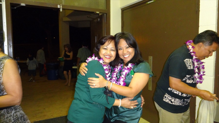 Two friends in leis hugging and laughing at an HBDA party
